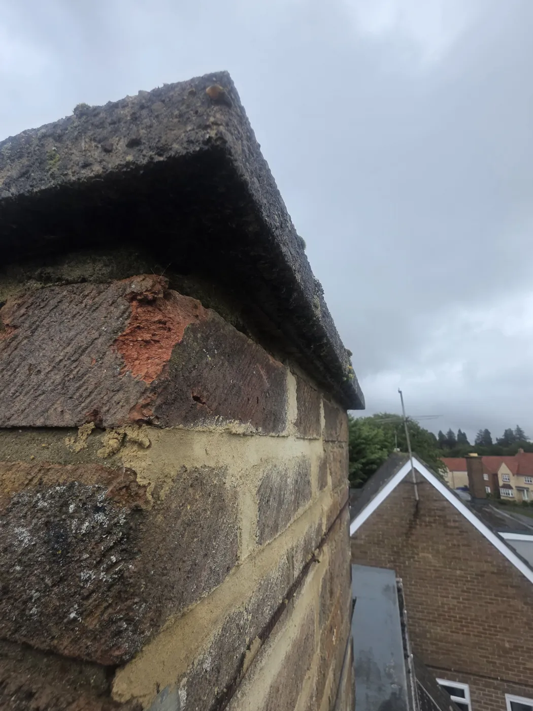 Crumbling brick and worn mortar just below the concrete cap of a chimney stack