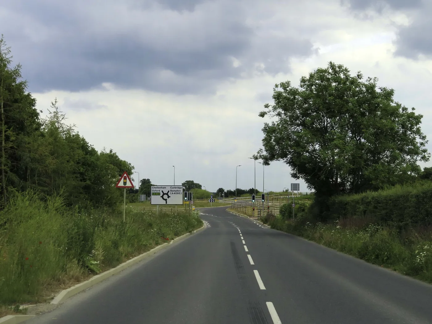 Downs Road approaching its junction with the A40 west of Witney. The appeal fixes access to the existing Downs Road roundabout.