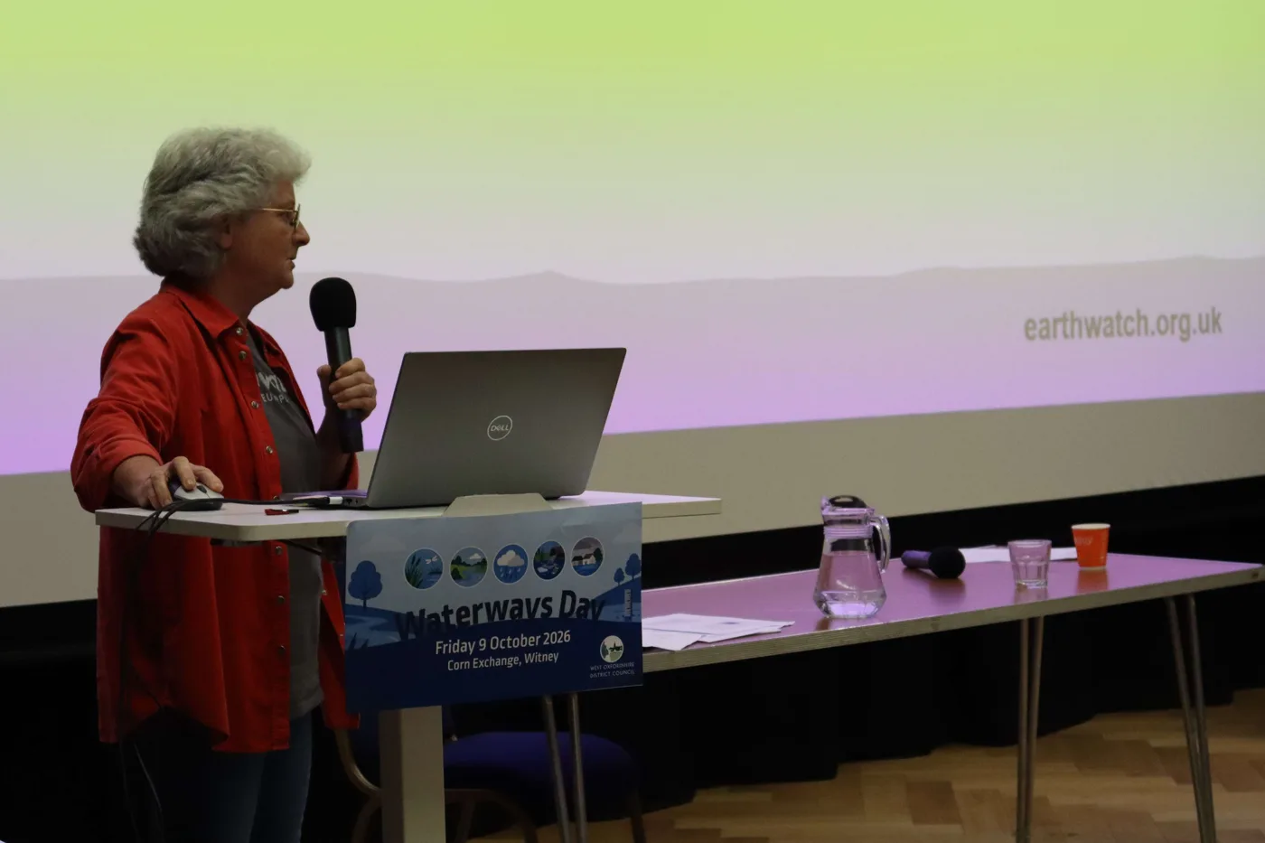 Dr Laura Bannatyne of Earthwatch speaking at the Waterways Day lectern, with earthwatch.org.uk on the screen behind her
